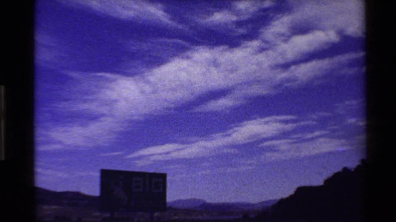 8mm road-trip view of a Big Wyoming billboard below a vivid purple-blue sky, with hills and open land in the distance.