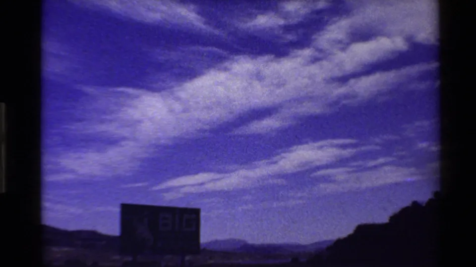 8mm road-trip view of a Big Wyoming billboard below a vivid purple-blue sky, with hills and open land in the distance.