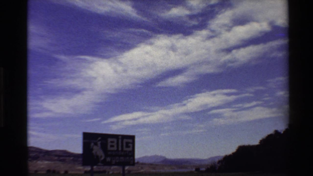 1980s 8mm Western USA frame showing a large "BIG wonderful wyoming" billboard in open countryside below streaky clouds.