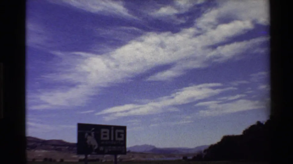 1980s 8mm Western USA frame showing a large "BIG wonderful wyoming" billboard in open countryside below streaky clouds.