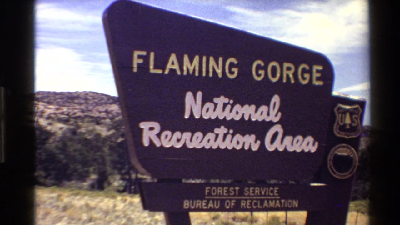 Handheld 1980 8mm view of the Flaming Gorge National Recreation Area roadside sign, with Forest Service shield and Bureau of Reclamation text visible.