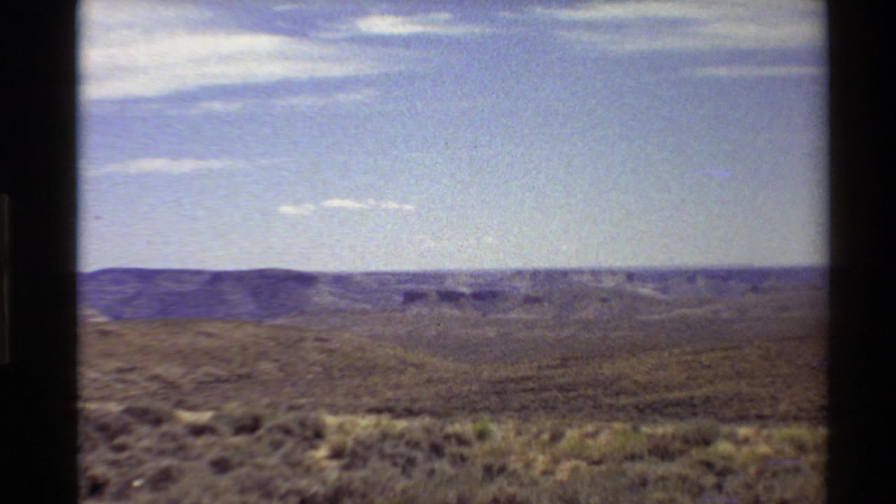 Wide arid canyon landscape under a blue sky with scattered clouds.