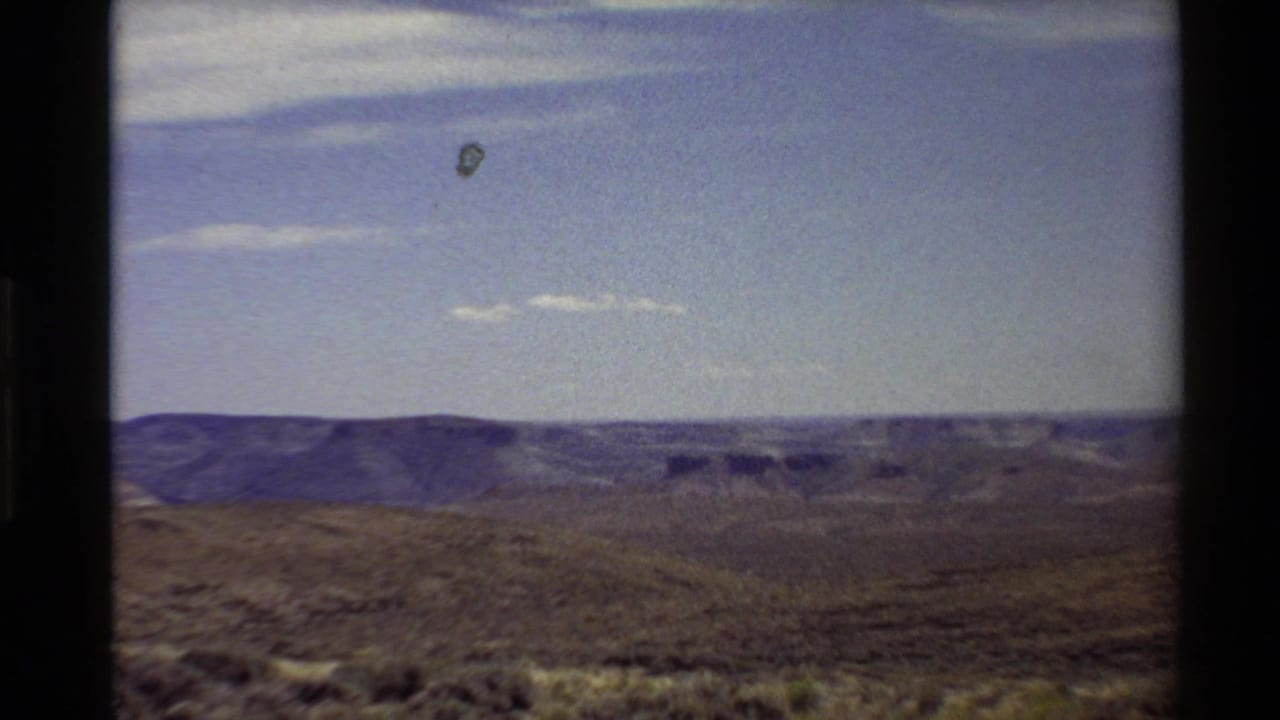Final 8mm frame of the western canyon vista near Flaming Gorge, with dark frame edges, blue sky, and distant rock formations.