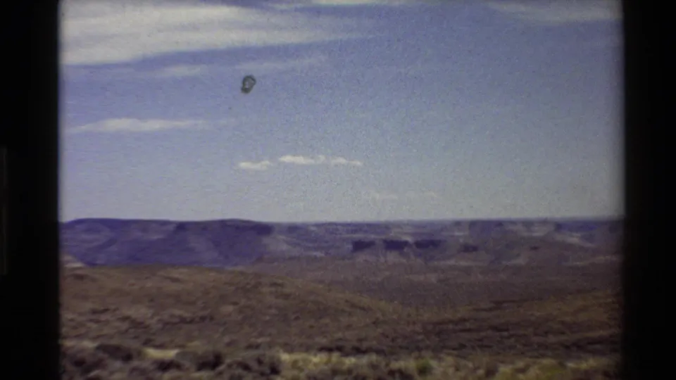 Final 8mm frame of the western canyon vista near Flaming Gorge, with dark frame edges, blue sky, and distant rock formations.