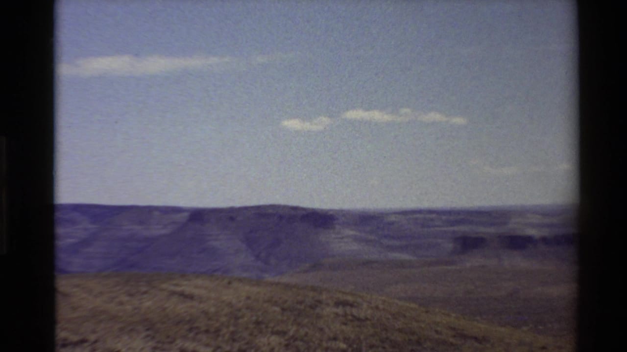 1980 Western U.S. home-movie frame showing layered ridges and dry grassland beneath a pale sky with dark film gate edges.