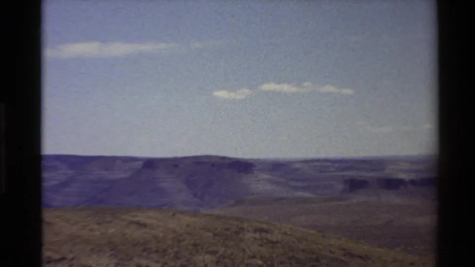 1980 Western U.S. home-movie frame showing layered ridges and dry grassland beneath a pale sky with dark film gate edges.