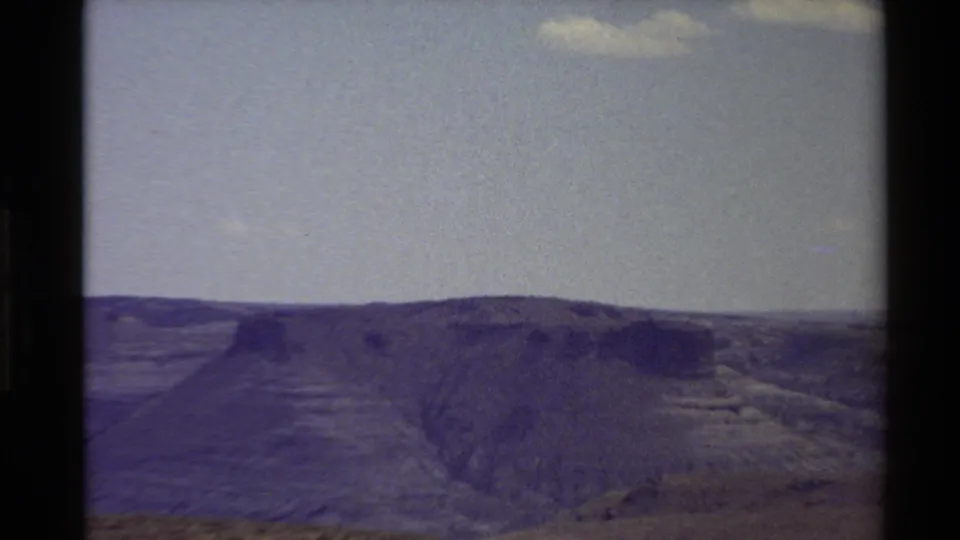 1980 Western U.S. 8mm frame with a broad ridge, sloped canyon terrain, and pale sky in a soft faded scan.