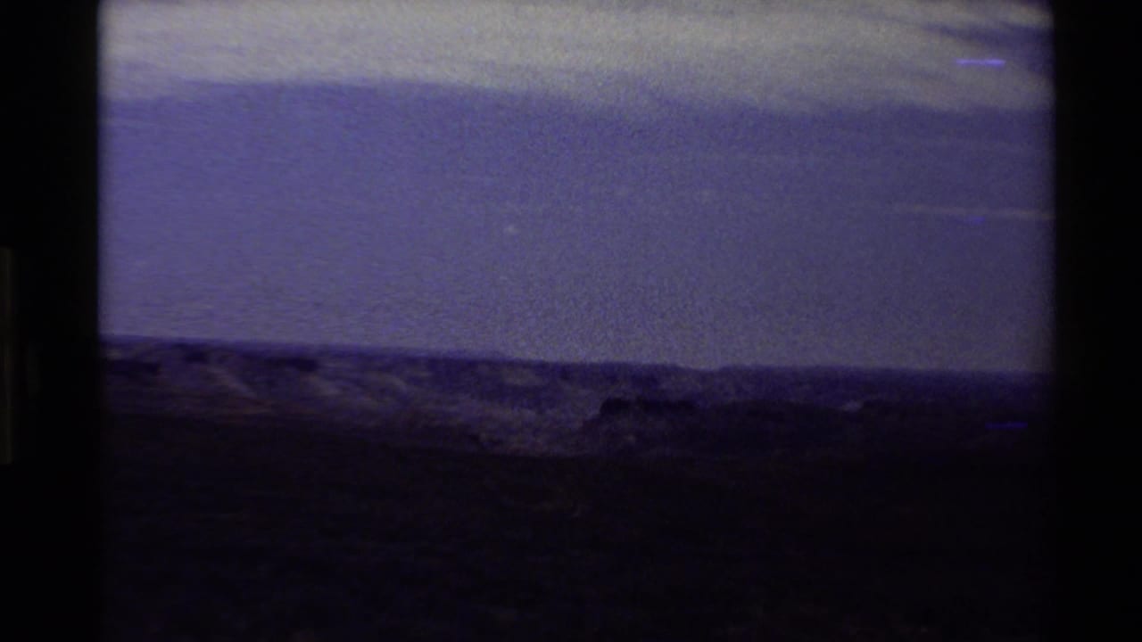 End-frame view from the 1980 8mm landscape clip, darkened with low ridge shapes and a strong blue-purple color shift.