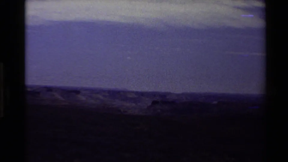 End-frame view from the 1980 8mm landscape clip, darkened with low ridge shapes and a strong blue-purple color shift.
