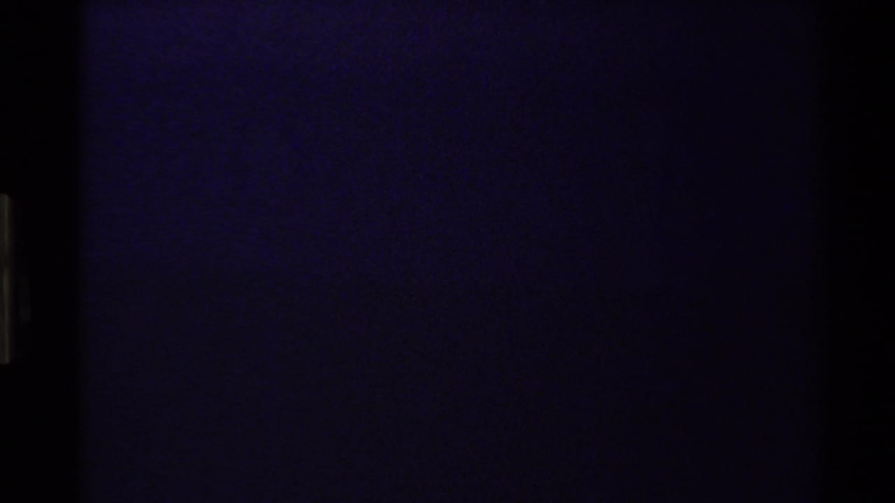 Dark 1980 Western USA 8mm frame with faint blue-purple light, heavy grain, and vertical film edge markings.