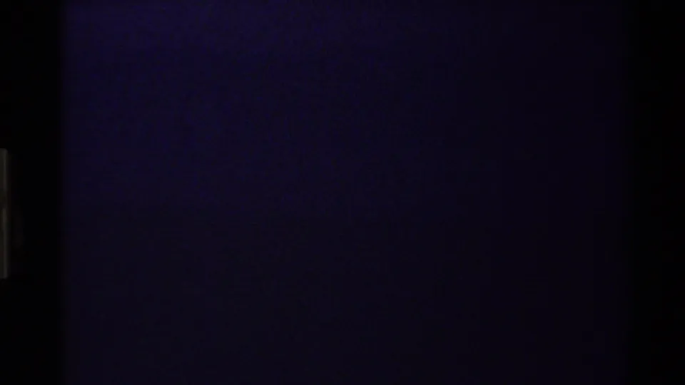 Dark 1980 Western USA 8mm frame with faint blue-purple light, heavy grain, and vertical film edge markings.
