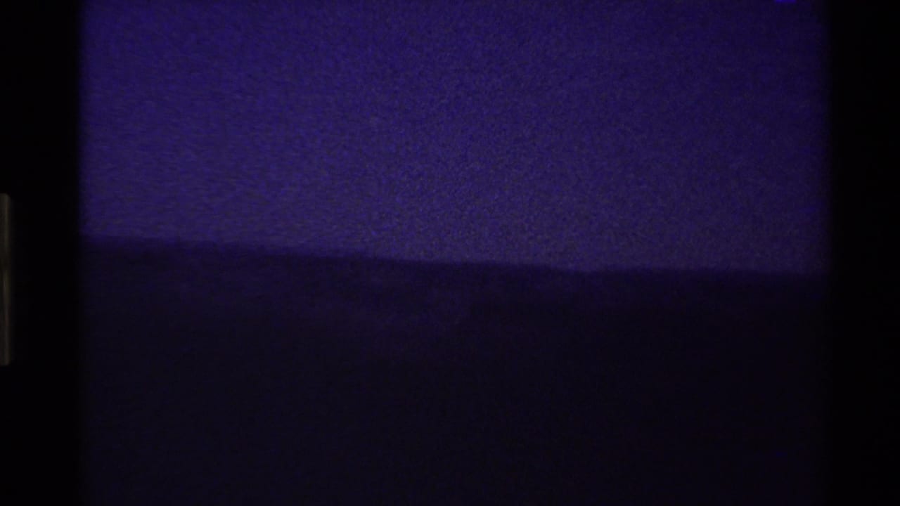 Dim purple sky above a dark mountain ridge with black film edge at left.