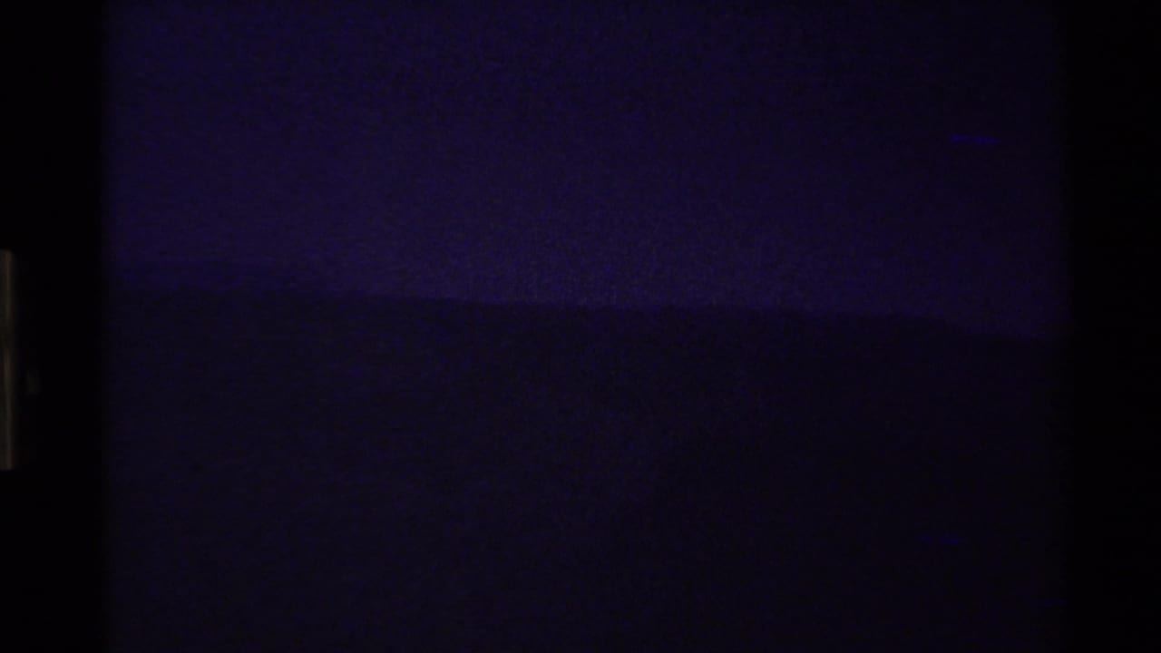 Grainy 1980 8mm frame with a mostly dark Western USA landscape and a faint purple horizon line.