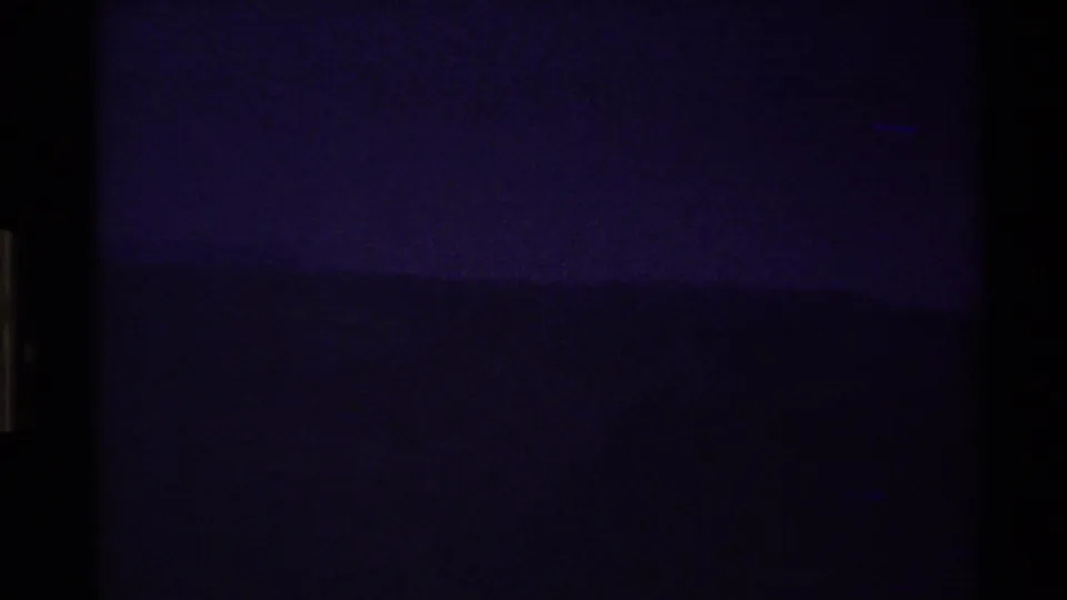 Grainy 1980 8mm frame with a mostly dark Western USA landscape and a faint purple horizon line.