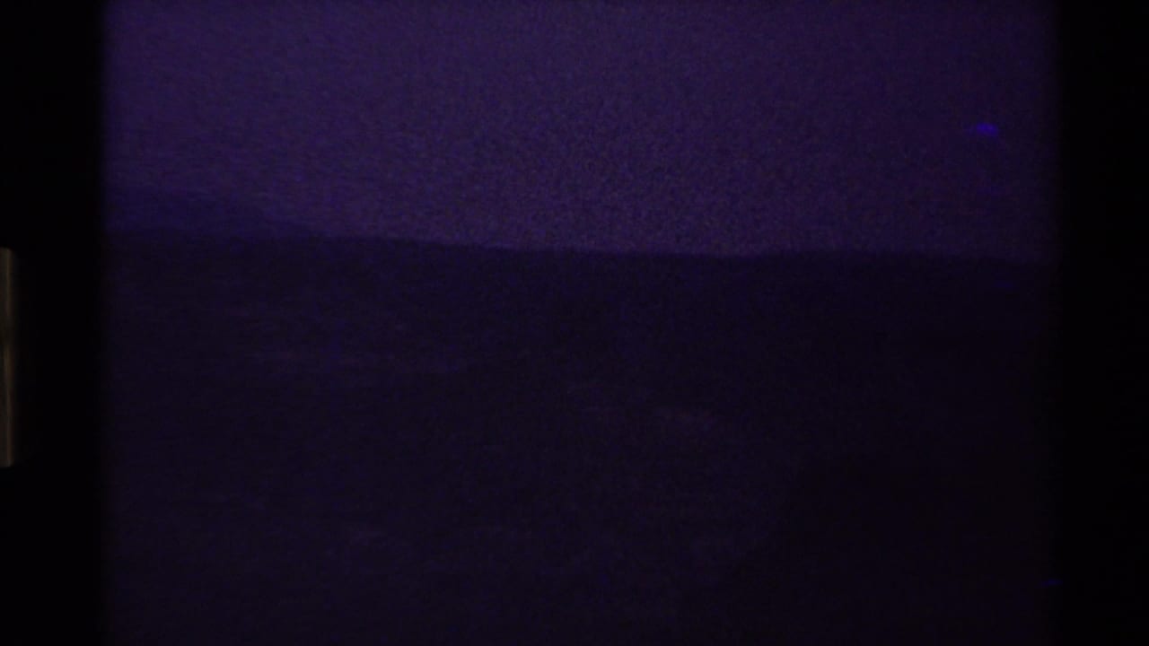 Dark underexposed film frame with a faint horizontal horizon or waterline.