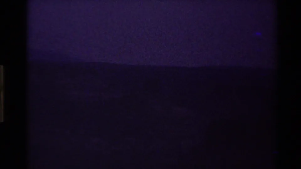 A mostly dark 8mm frame at the start of the clip, with faint purple-blue exposure and a barely visible landscape line.