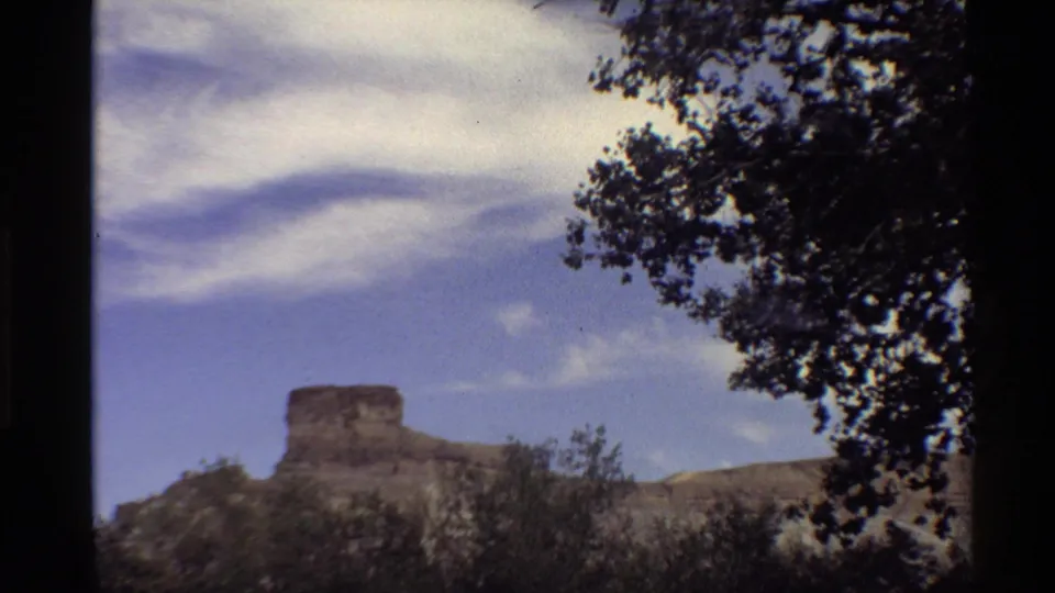 A second handheld 8mm view holds on the Western U.S. rock formation, with brushy terrain below and dark foliage along the upper right.