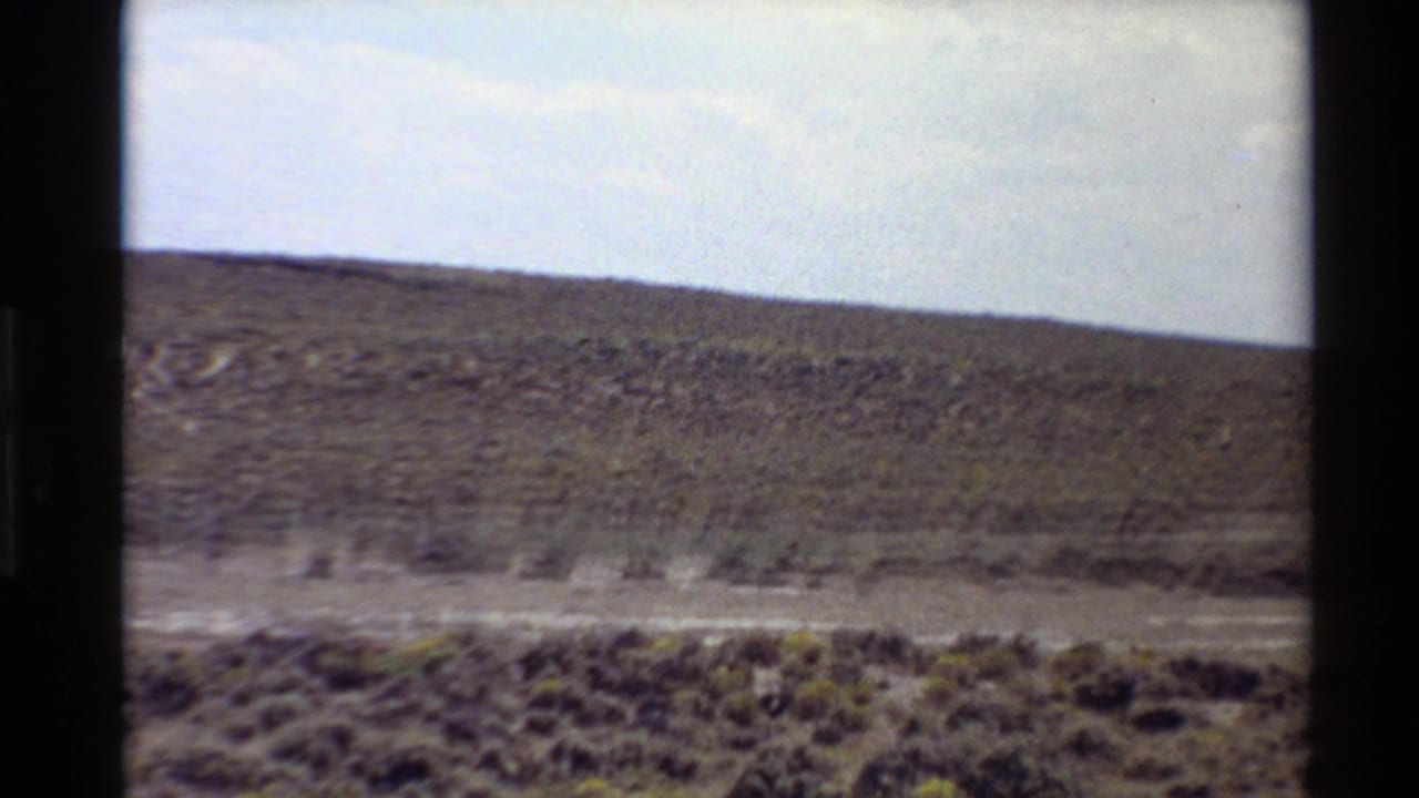 1980 Western U.S. home-movie frame showing small antelope running across open scrub grassland beneath low hills.