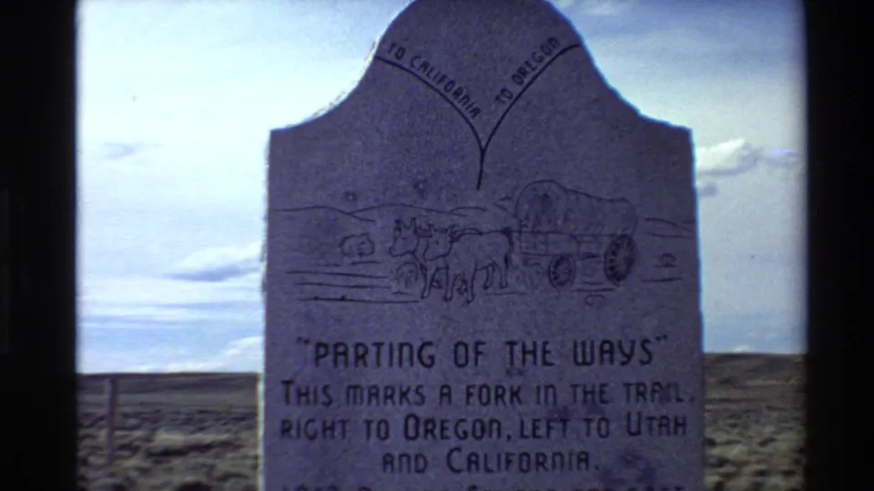 A stone "Parting of the Ways" trail marker stands in open desert, with text directing routes toward Oregon, Utah, and California.