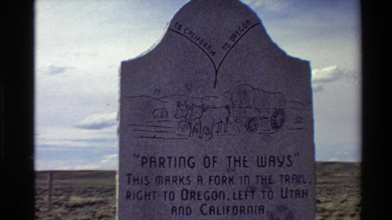 Stone trail marker with wagon carving and directional text in a plains setting.