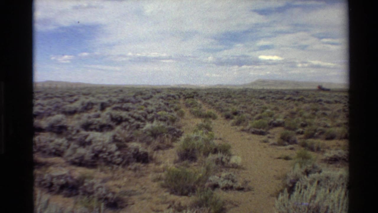 Wide 1980 8mm view across arid Western USA sagebrush plains with a faint track and distant low hills.