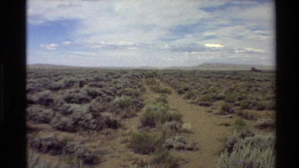 Wide 1980 8mm view across arid Western USA sagebrush plains with a faint track and distant low hills.