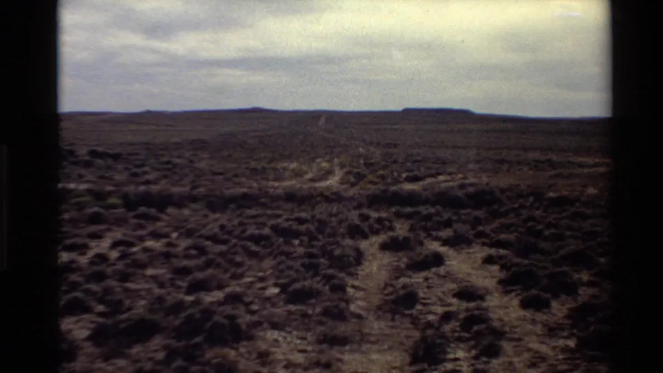 Wide 1980 8mm desert landscape in the Western United States, showing scrubland and a faint track toward distant mesas or hills.