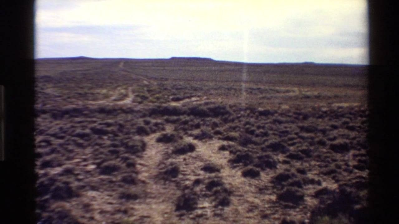 1980 8mm frame of Western U.S. scrub desert, showing branching tracks across open ground toward low distant hills.