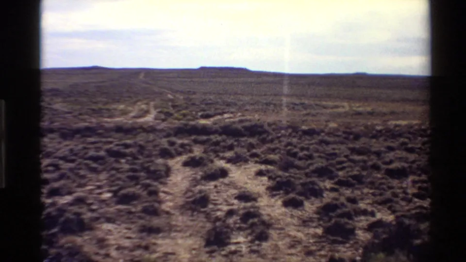 1980 8mm frame of Western U.S. scrub desert, showing branching tracks across open ground toward low distant hills.