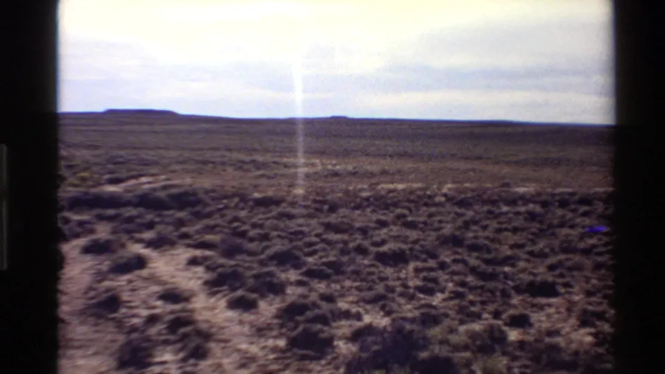 Western U.S. 1980 home-movie frame showing flat arid scrubland, distant low landforms, and visible film gate borders.