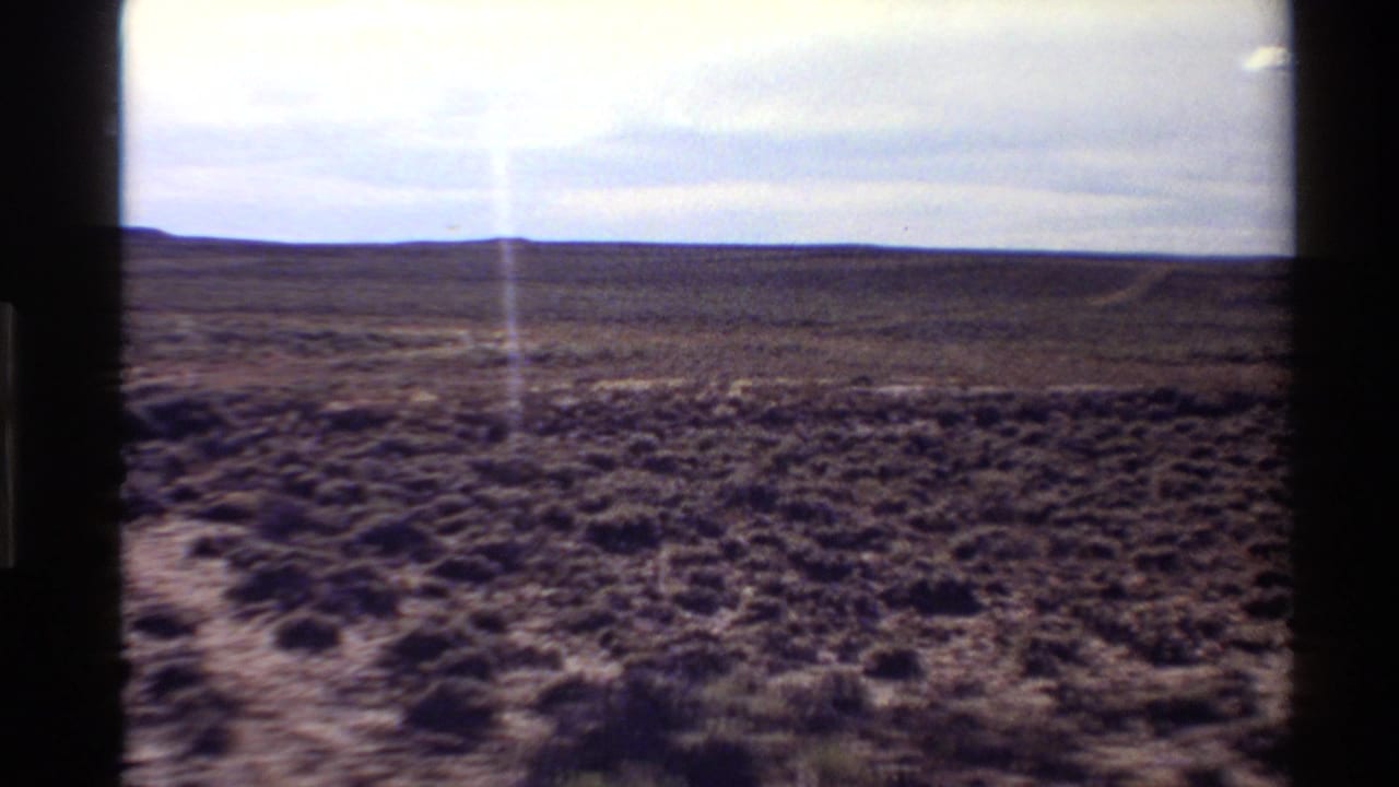 1980 8mm frame of arid Western U.S. scrubland with a low horizon and prominent vertical light flare in the film image.