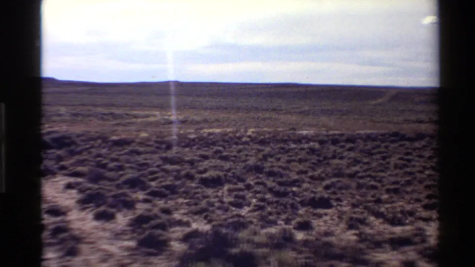 1980 8mm frame of arid Western U.S. scrubland with a low horizon and prominent vertical light flare in the film image.