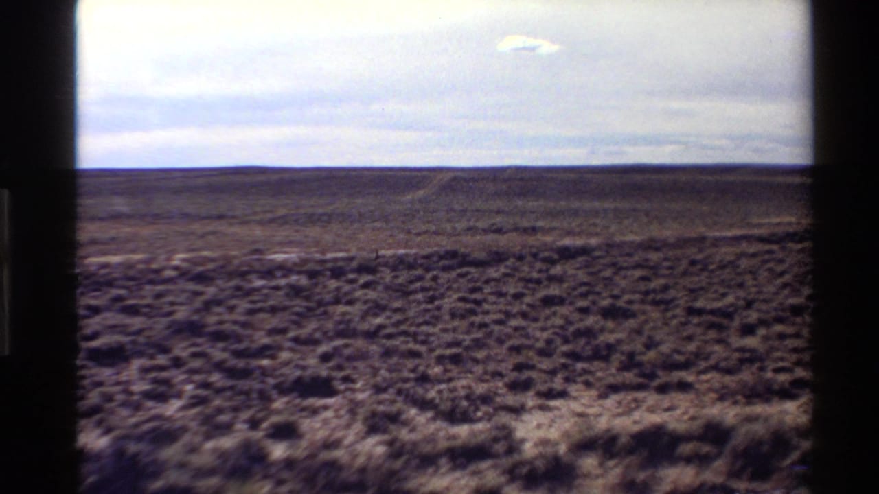 1980 Western U.S. 8mm view of open desert scrub and a low horizon beneath a cloudy sky, seen through dark frame edges.
