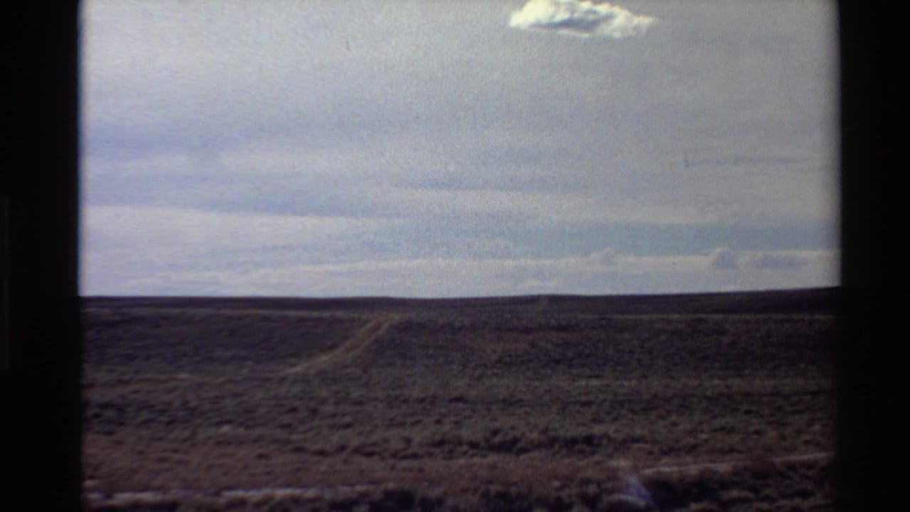 1980 Western USA 8mm frame showing open arid ground beneath a pale blue sky and a single small cloud.
