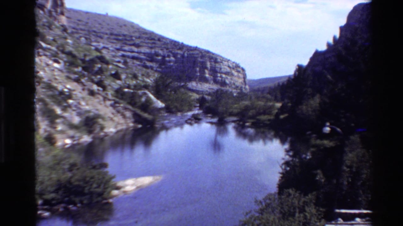The final frame looks across quiet river water toward layered canyon rock and trees in 1980 Western U.S. footage.
