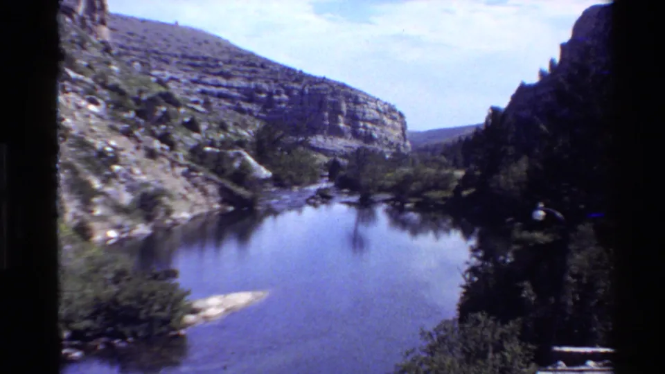 The final frame looks across quiet river water toward layered canyon rock and trees in 1980 Western U.S. footage.