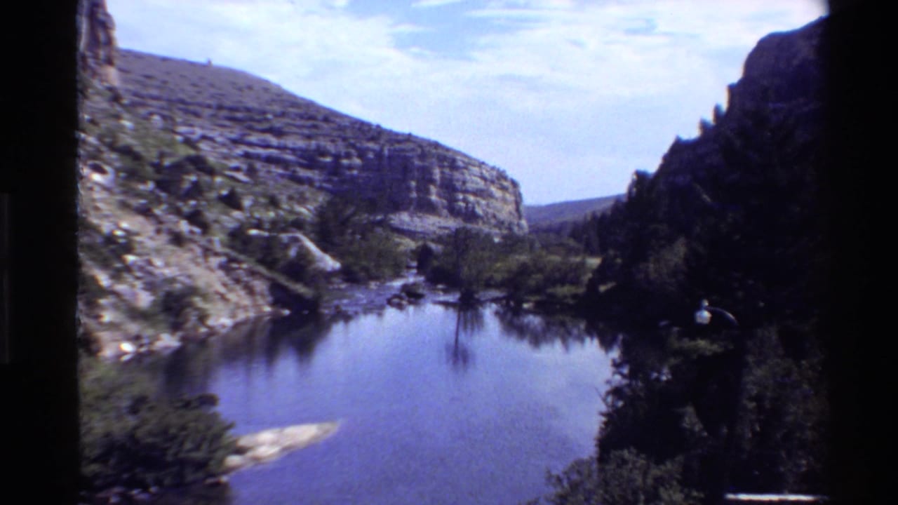 1980 home-movie view of a mountain lake or river bend between rugged canyon walls in the Western United States.