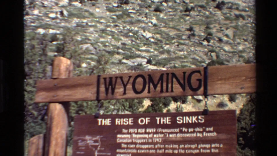 Visitor-shot 1980 footage of a wooden Wyoming sign and Rise of the Sinks panel against a rocky hillside.