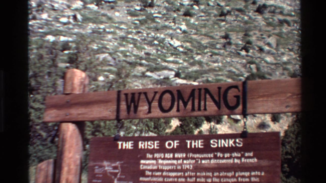 1980 8mm home-movie frame of a wooden Wyoming sign and The Rise of the Sinks interpretive plaque in rugged terrain.