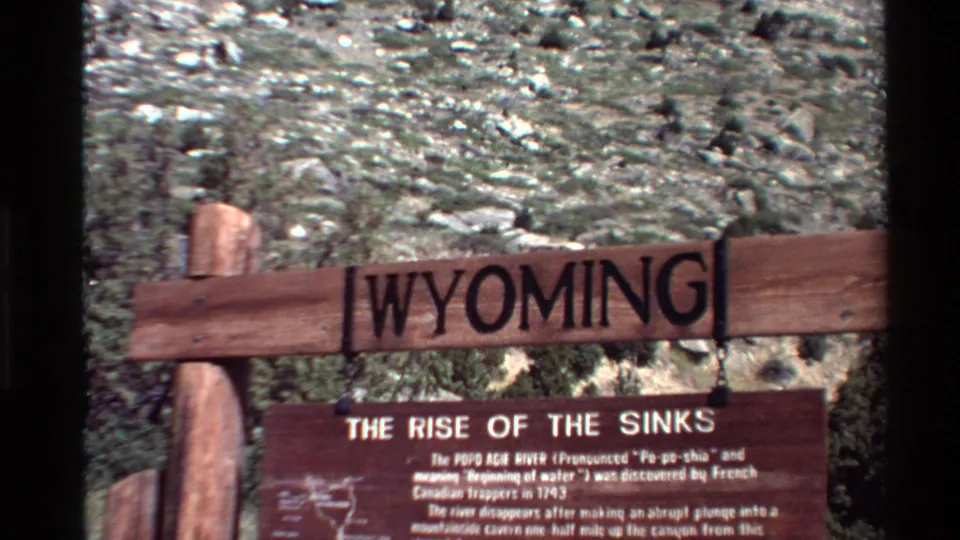1980 8mm home-movie frame of a wooden Wyoming sign and The Rise of the Sinks interpretive plaque in rugged terrain.
