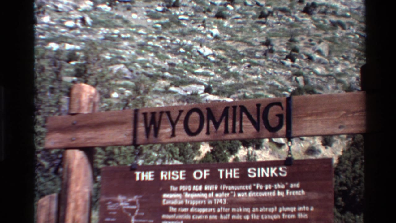 Wooden Wyoming sign above a Rise of the Sinks plaque on a rocky hillside.