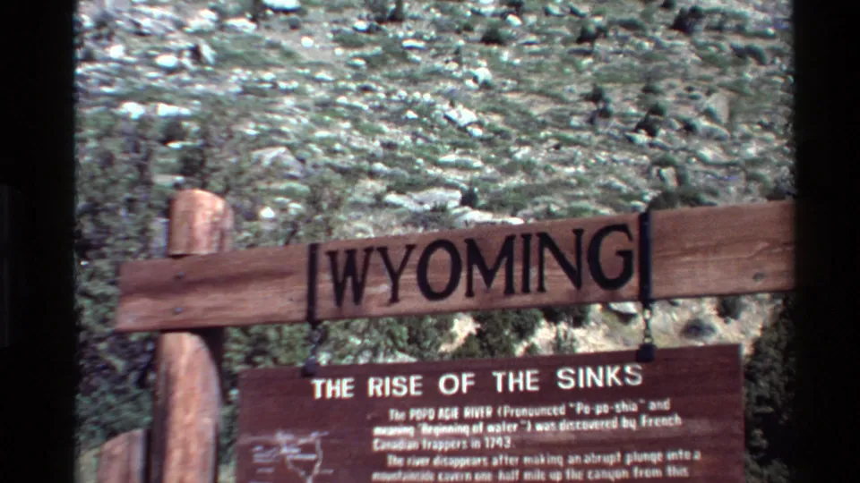 Slightly shifted 8mm frame showing the carved Wyoming sign above the Rise of the Sinks plaque at the natural landmark.
