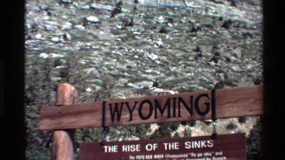 Final 1980s home-movie frame of the Wyoming sign and Rise of the Sinks plaque, with arid rocky terrain behind.