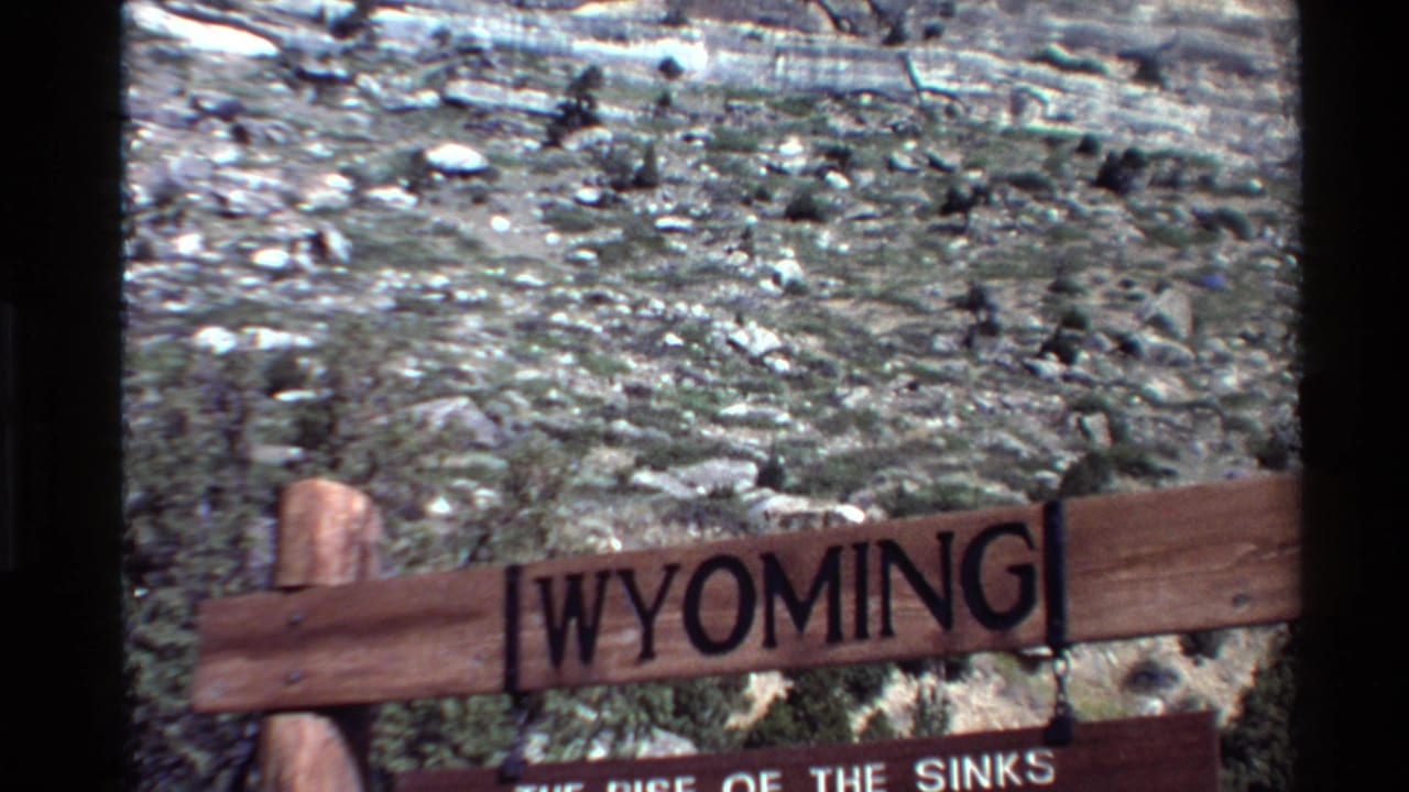 1980 8mm frame showing a wooden Wyoming sign with partial site text before a layered rocky landscape.