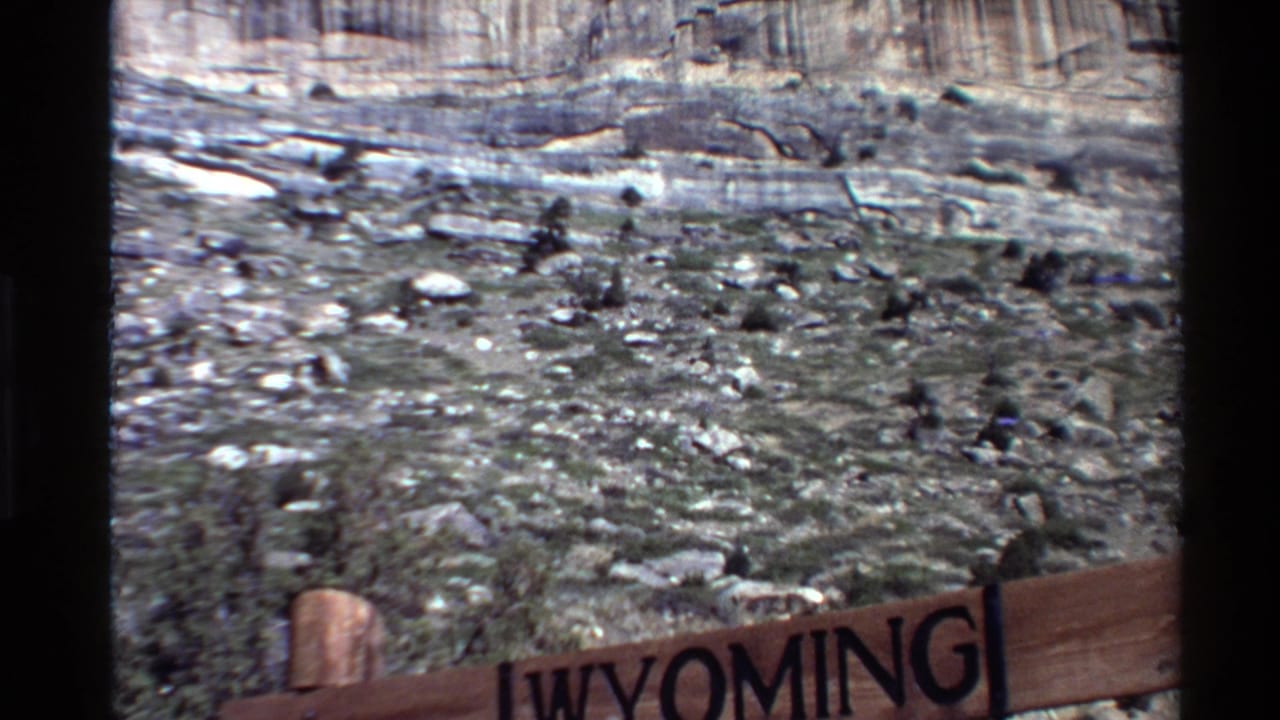 Partial Wyoming sign at the lower edge with rocky slope and cliff behind it.