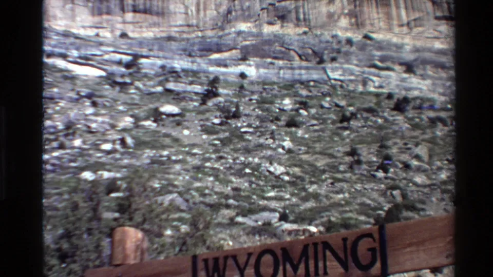 Visitor-shot 8mm view with the Wyoming sign partly cropped below a rocky slope and banded cliff wall.