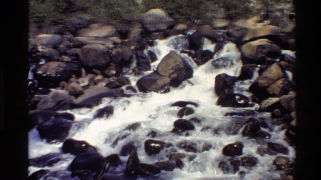 Whitewater stream rushing over dark rocks and large brown boulders.