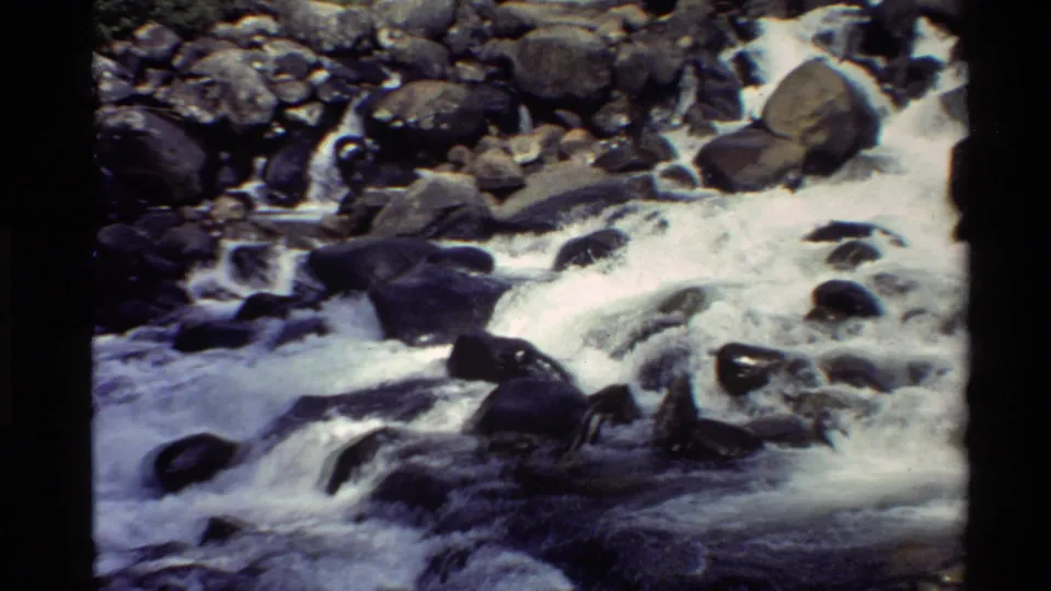 Fast water runs through a boulder-filled channel in this 1980 Western U.S. home-movie frame.