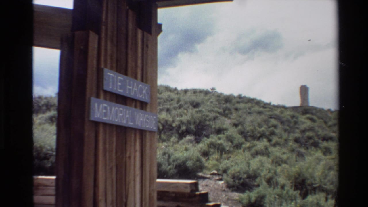 Wooden Tie Hack Memorial Wayside sign beside a brushy hillside and distant tower.