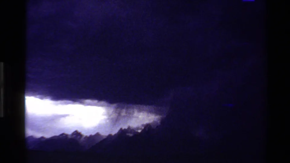 1980 Western U.S. 8mm view of heavy blue-purple storm clouds over jagged mountain peaks and a bright break in the sky.